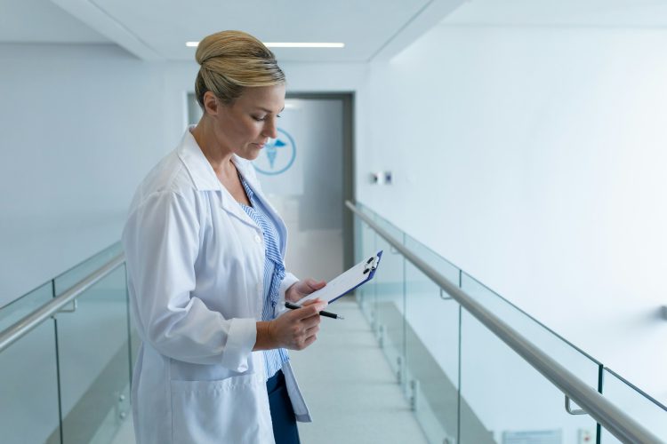 Caucasian female doctor standing in hospital corridor looking at medical chart document