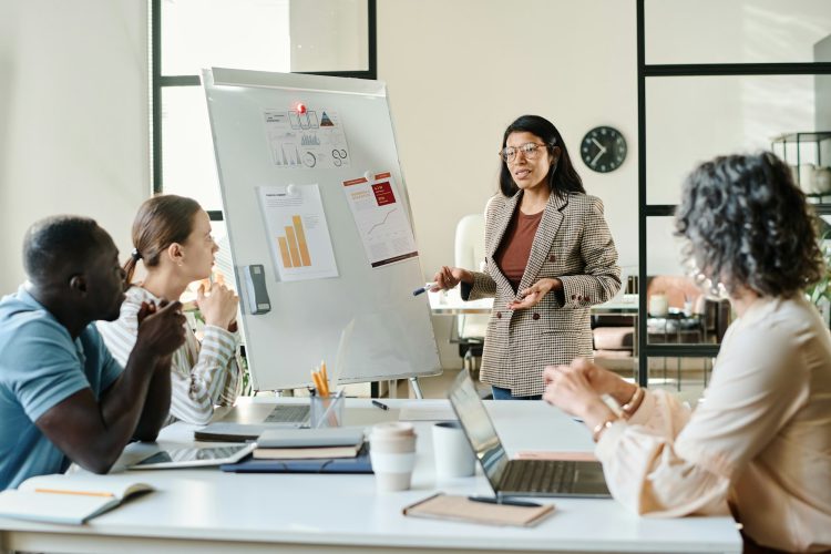 Young confident economist standing by whiteboard in front of colleagues